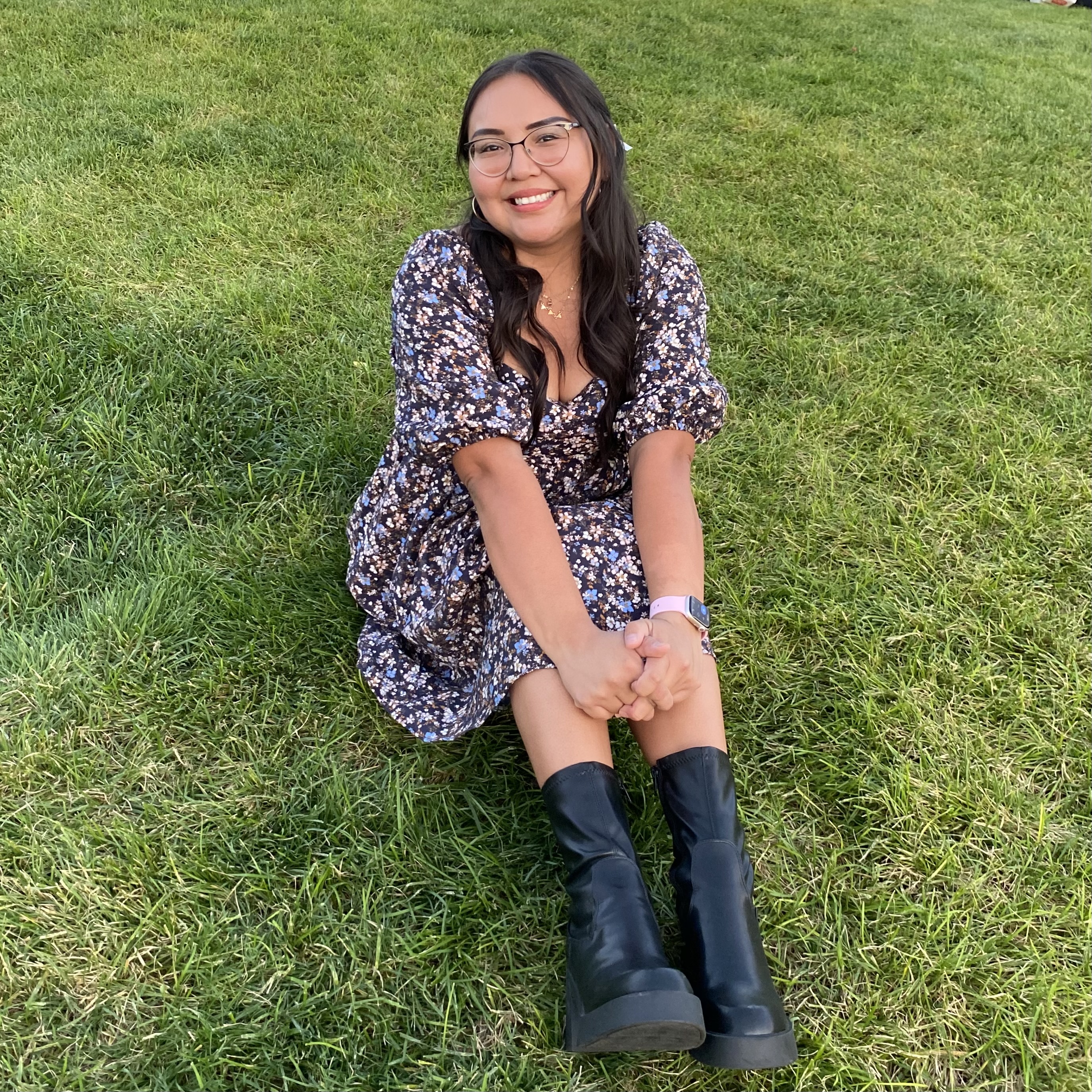 Evelyna sits smiling in a floral dress on green grass